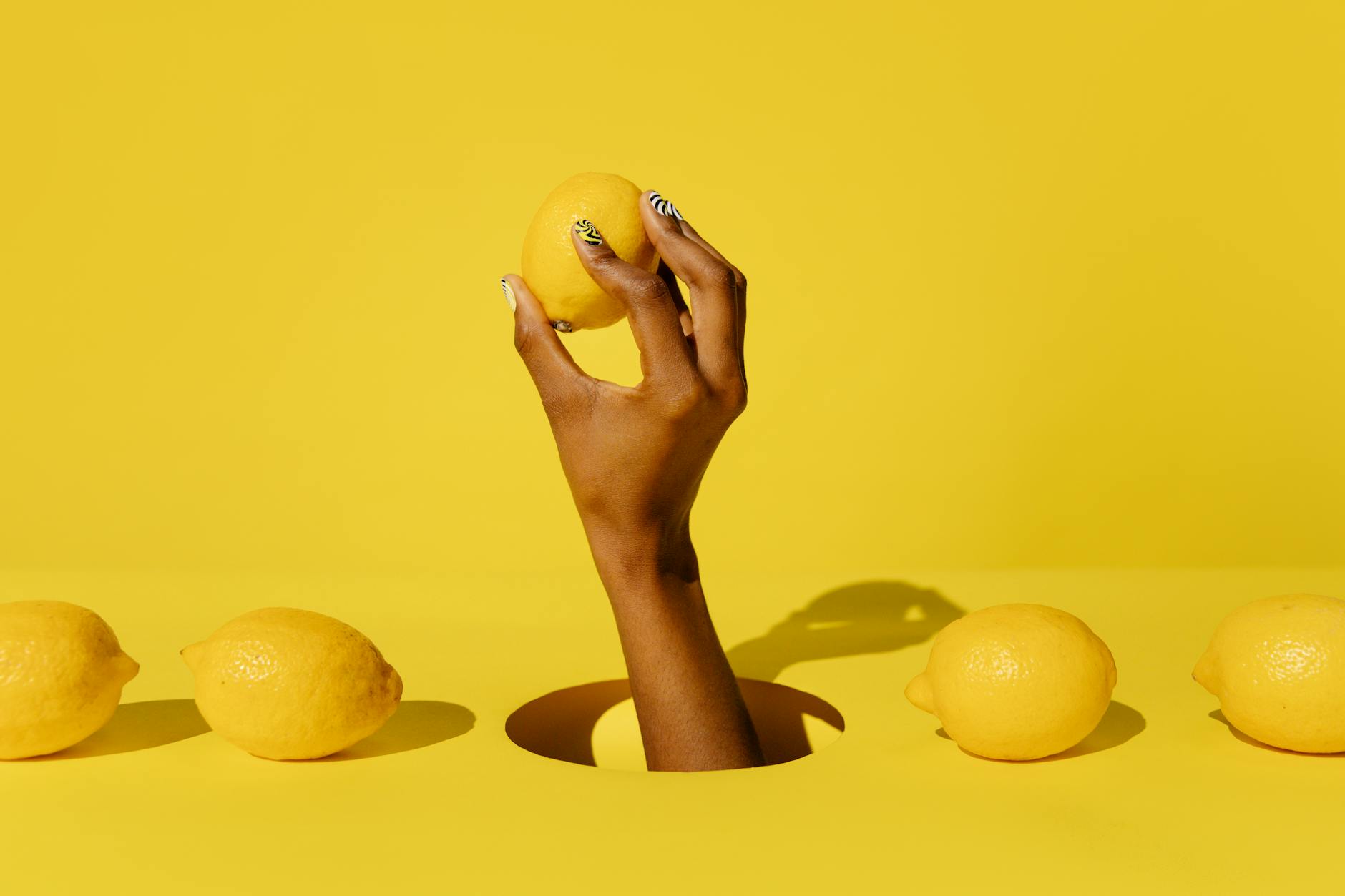 A hand holding a fresh lemon against a vivid yellow background, conveying freshness and citrus energy