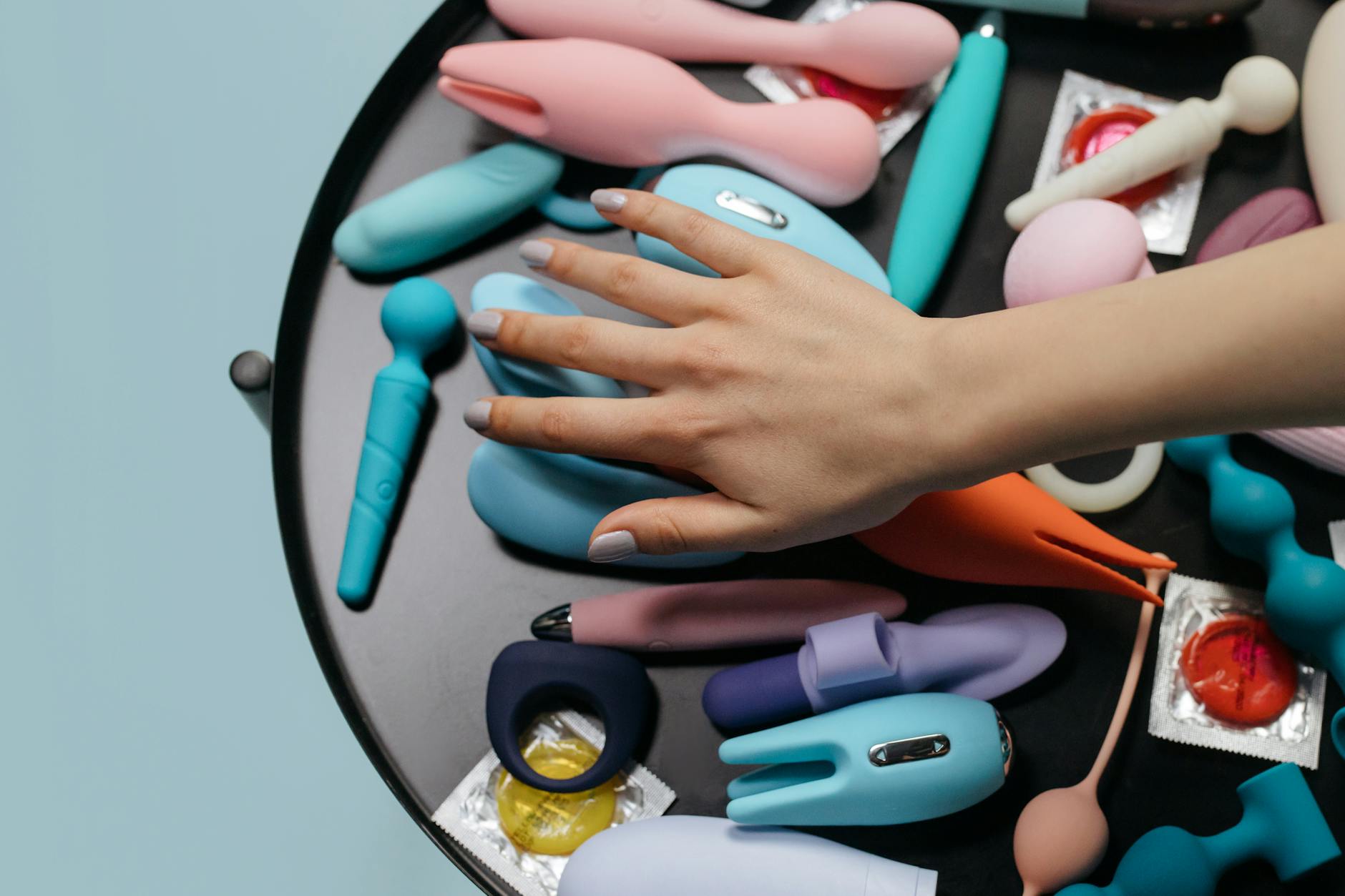 Woman holding blue and pink clitoral vibrators in a thoughtful moment