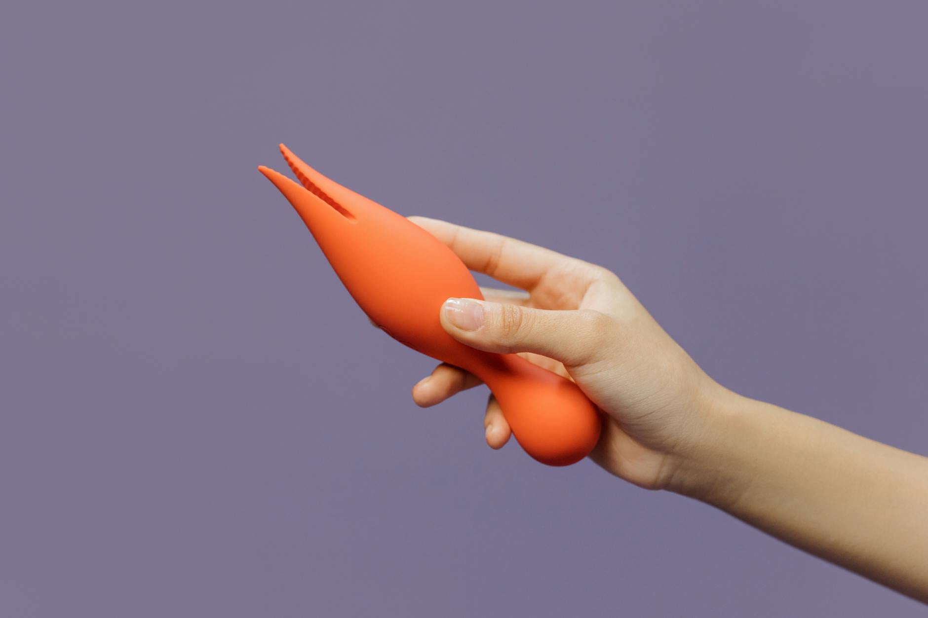 A hand holding a lemon-colored clitoral vibrator against a minimalist purple backdrop.