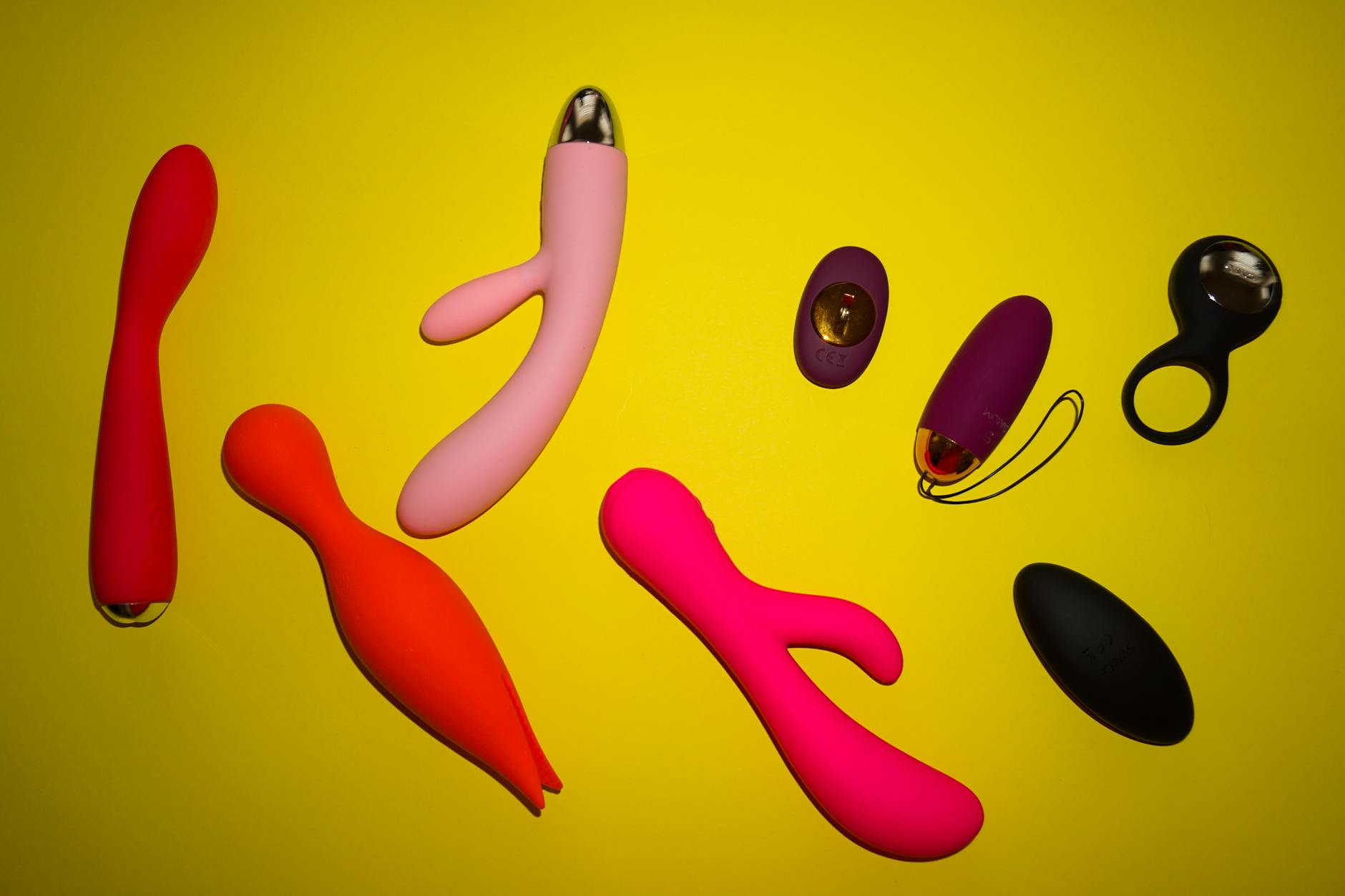 Vibrant array of colorful sex toys on a bright yellow surface, representing diverse pleasure options and creative exploration.
