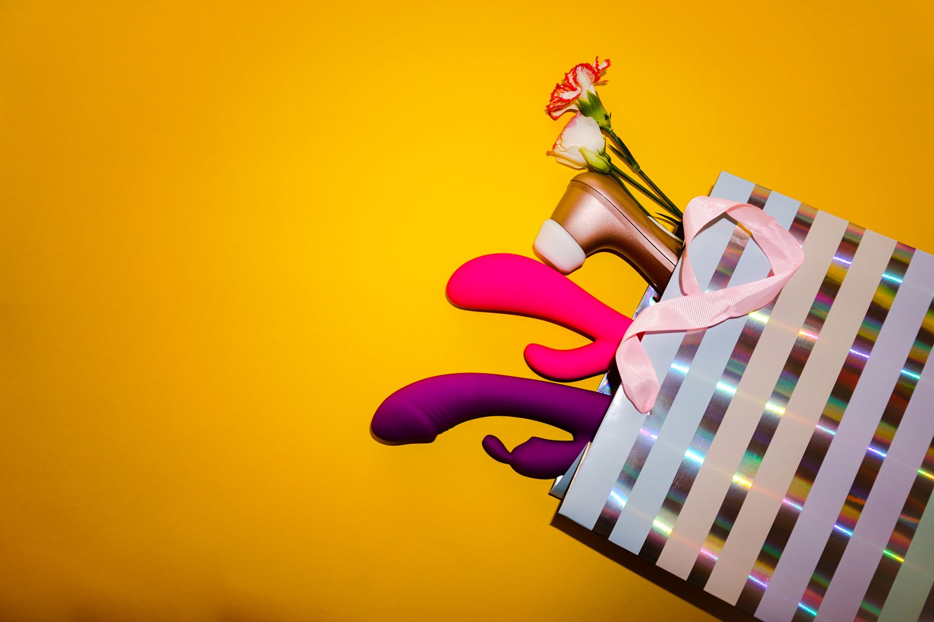 Yellow silicone vibrator surrounded by fresh bananas on a bright yellow background