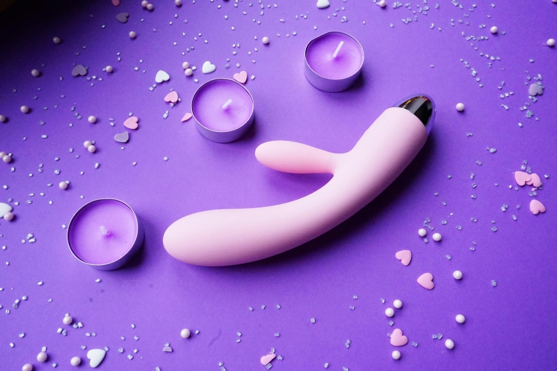 Pink vibrator on a purple background with romantic lighting and confetti